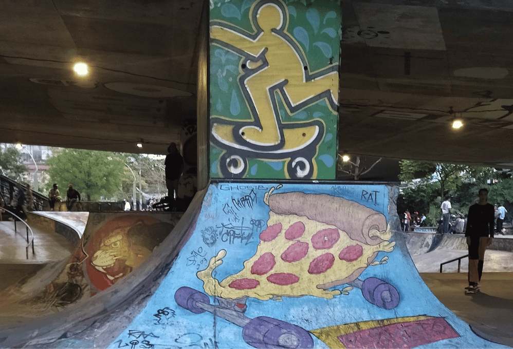 Grafiti de pizza en la pista de skate del sector del Puente de la 4 Sur, Medellín: un espacio donde personas de diversas edades se reúnen para compartir experiencias, consumir marihuana y participar en eventos artísticos. Este lugar ha evolucionado como un punto de encuentro cultural, fusionando arte urbano, música y libertad de expresión en un ambiente alternativo que refleja la creatividad y la identidad local.